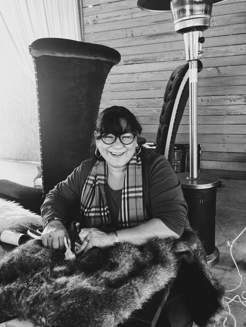 Smiling woman in a cozy setting, crafting with fabric and thread, surrounded by furniture. Showcases craftsmanship and a warm atmosphere.