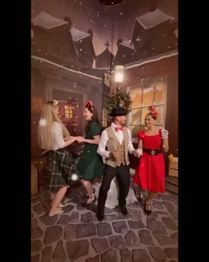 A festive group dances in a charming, snow-covered outdoor setting, wearing colorful holiday outfits, celebrating the joyful atmosphere of the season.
